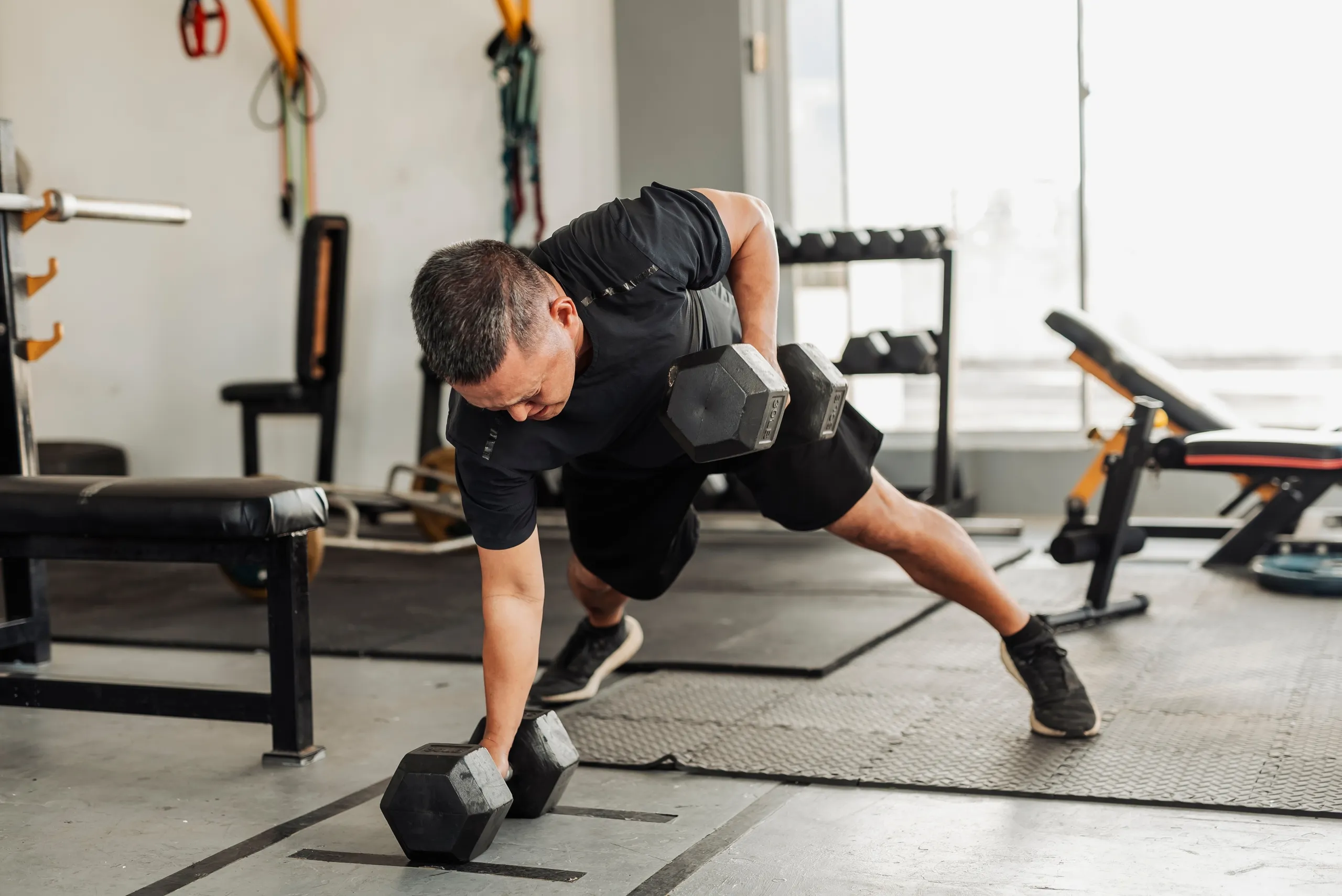 Strength training with dumbbells: Men performing the Renegade Row exercise at the gym.